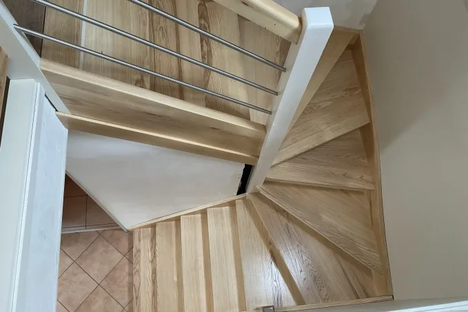 Escalier double quart tournant en bois clair avec contremarches, marches balancées et lisses inox vu d'en haut.