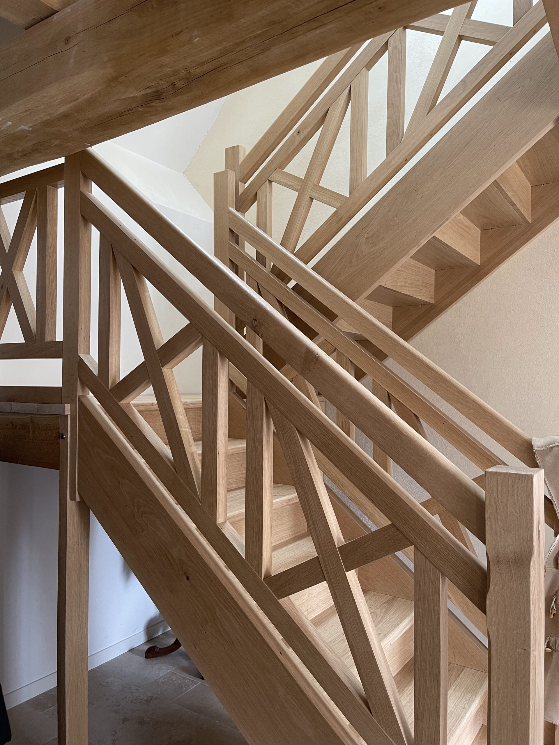 Escalier sur mesure en bois massif avec palier, limon entaillé et garde-corps motifs croix de Saint-André.